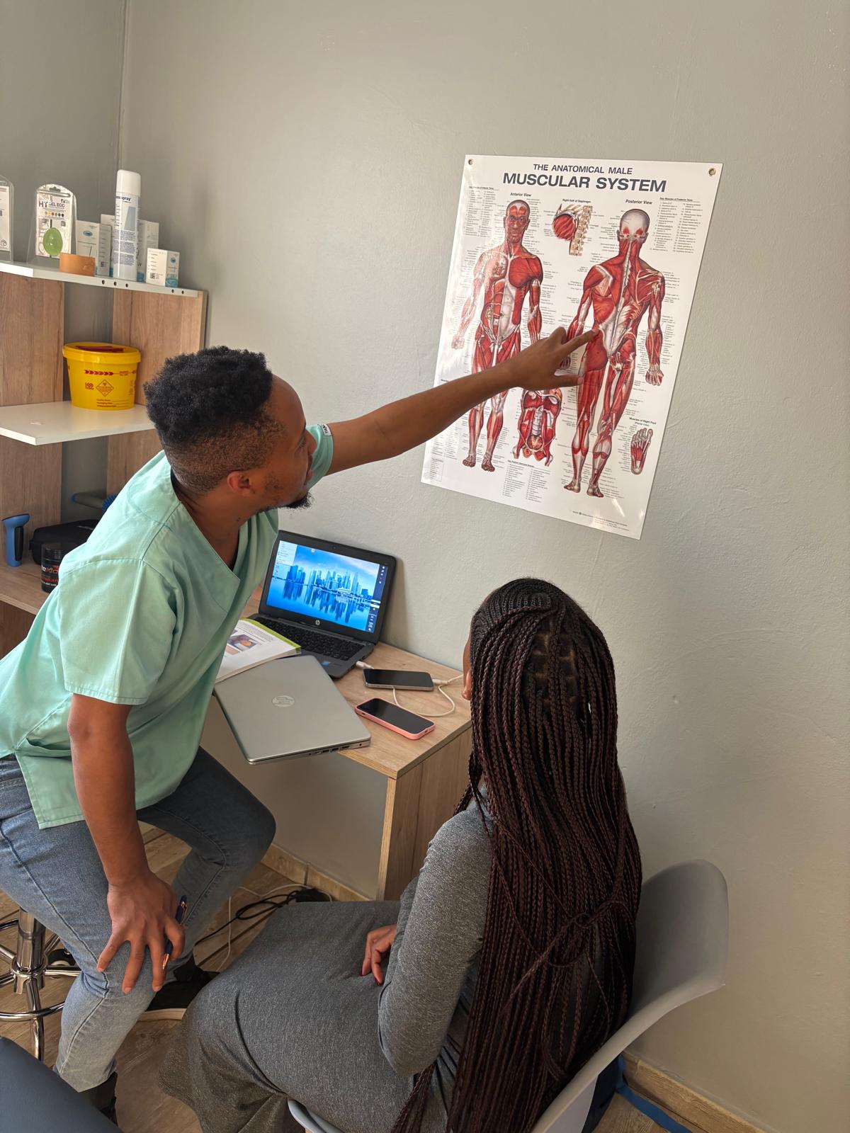 Sipho explaining muscle anatomy to a patient using a wall chart